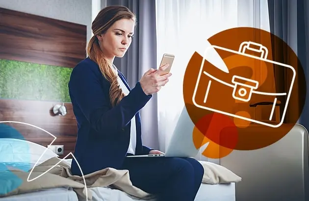 Üzletasszony telefonnal ül a szállodai ágyon, mellette aktatáska ikon