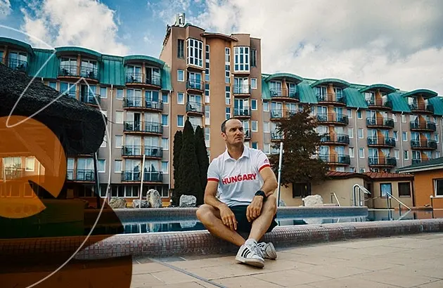 Kuttor Csaba a medence szélén ül, mögötte a szálloda