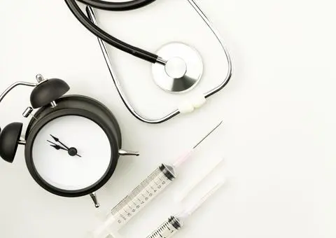 Ébresztőóra, sztetoszkóp és fecskendő fehér háttéren